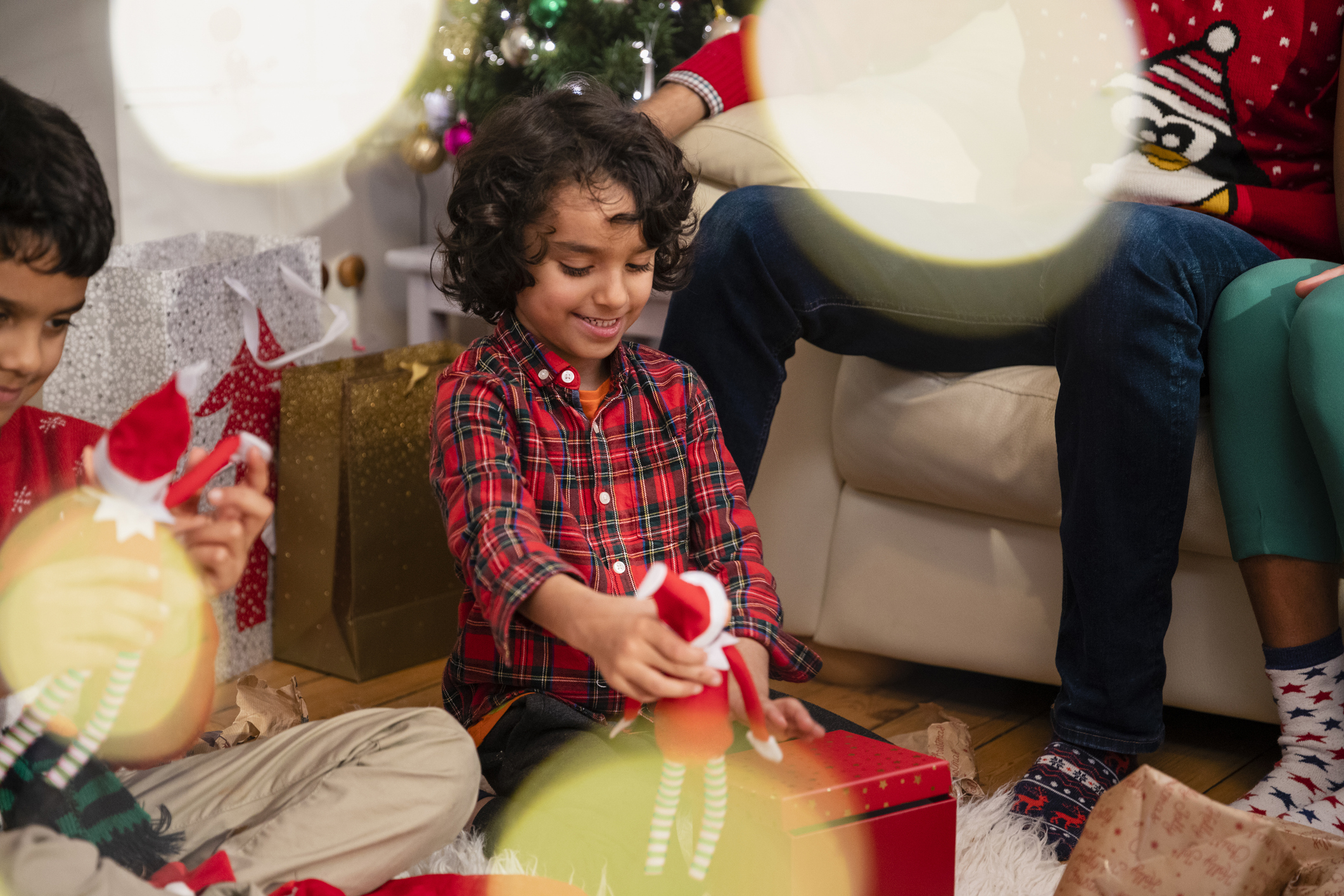 Shot of a family with two sons opening Christmas presents on Christmas morning in the Northeast of England. Their parents are sitting on the sofa watching the children unwrap their gifts.