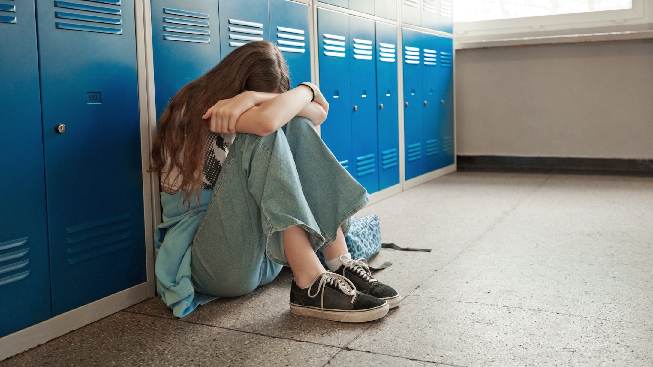 sad female dent sitting on floor next to lockers at school.