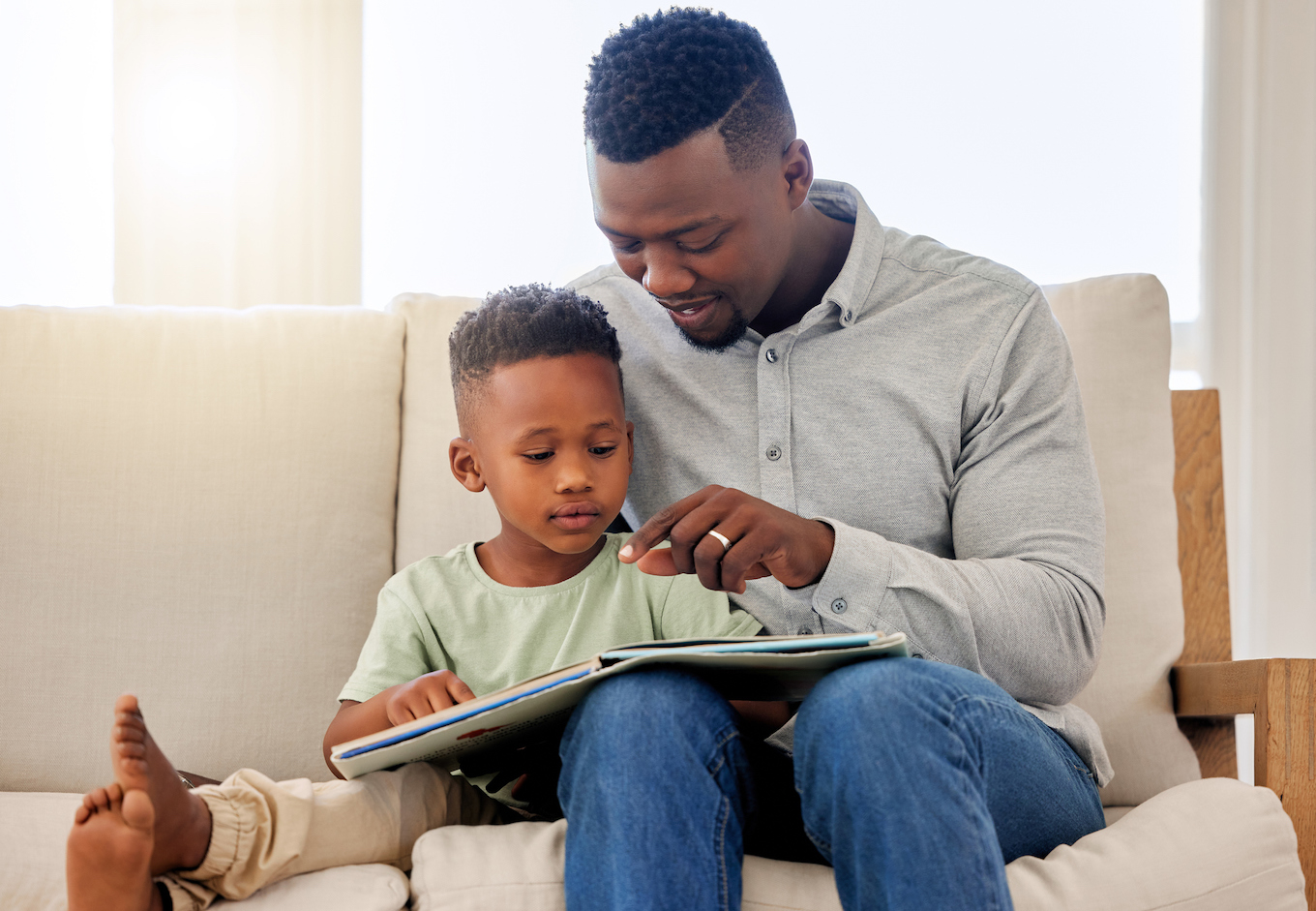 African, child and father reading a book in home on sofa with development of education, learning and knowledge. Happy dad, teaching and show kid a story in books and relax in living room on couch