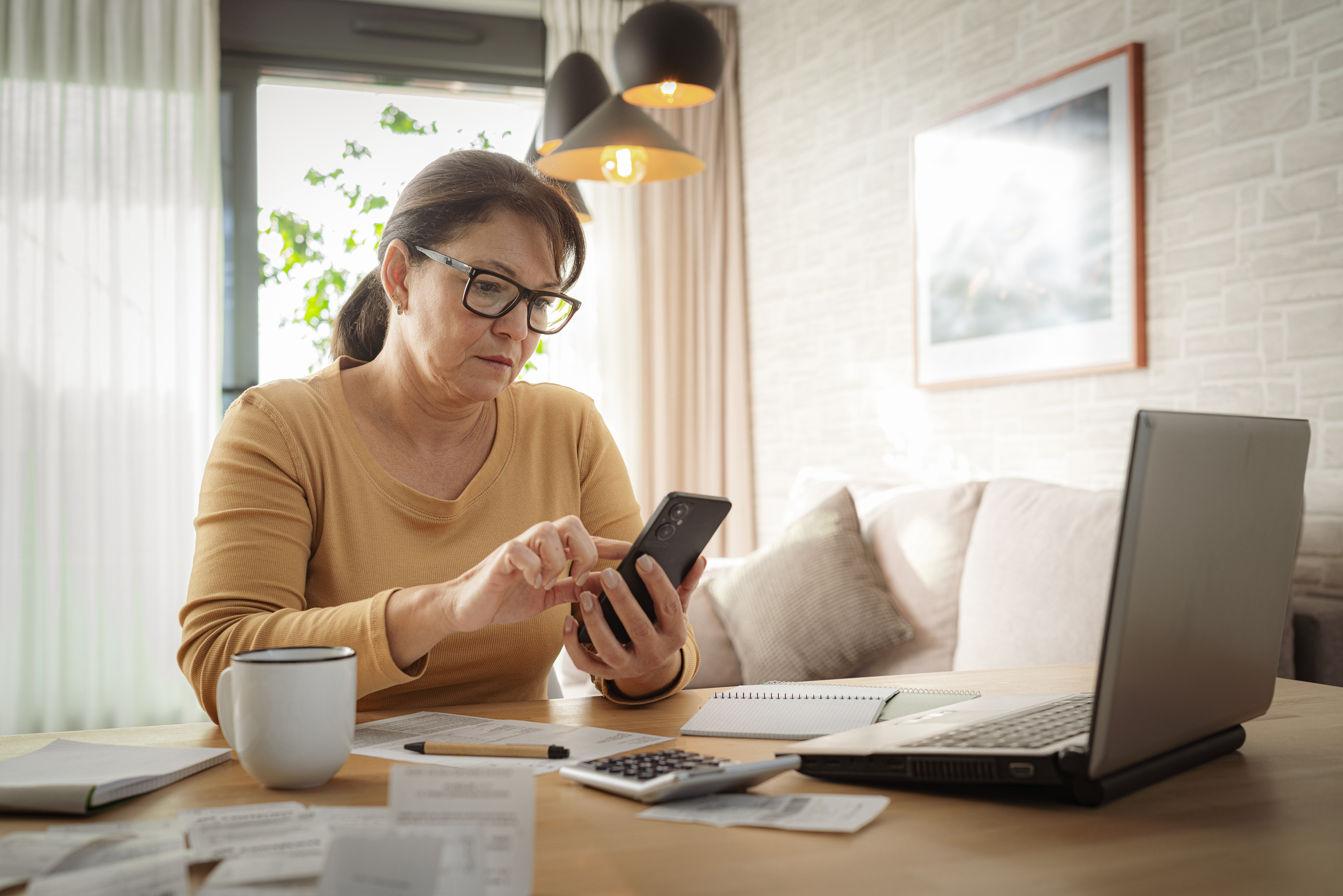 Woman using mobile phone and laptop working from home. Home finances. Calculating budget. Preparing taxes investing